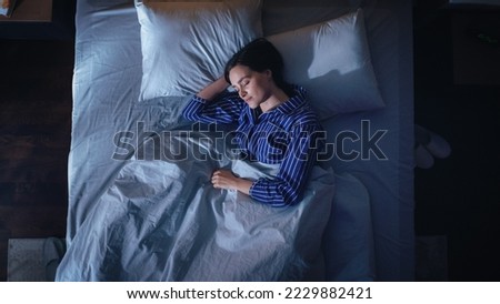 Top View of Beautiful Young Woman Sleeping Cozily on a Bed in Her Bedroom at Night. Comfortable Apartment with Sweet Girl Resting when Moonlight Shining Through Apartment Window. Top Down Royalty-Free Stock Photo #2229882421