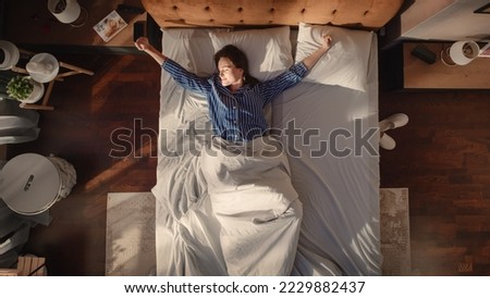Top View Apartment: Beautiful Young Woman Sleeps Charmingly in Her Bed, Turns off Smartphone Alarm Clock, Greets a New Day with Happiness and Smiles. Top Down Royalty-Free Stock Photo #2229882437
