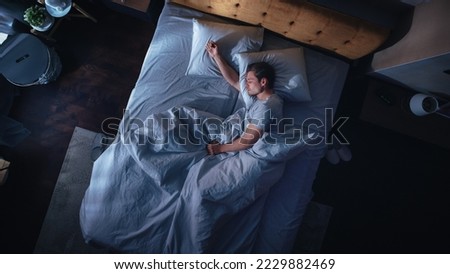 Top View Apartment Bedroom: Handsome Young Man Sleeping Cozily on a Bed in His Bedroom at Night. Comfortable Apartment with Guy Resting for Productive next Day. Top Down Above Royalty-Free Stock Photo #2229882469