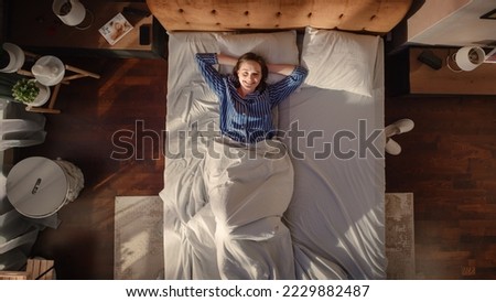 Top View Apartment: Beautiful Young Woman Sleeps Charmingly in Her Bed, Turns off Smartphone Alarm Clock, Greets a New Day with Looking at Camera and Smiling. Top Down Royalty-Free Stock Photo #2229882487