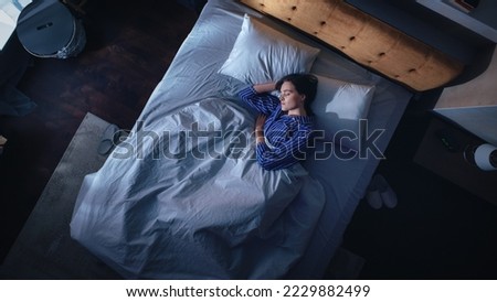 Top View of Beautiful Young Woman Sleeping Cozily on a Bed in Her Bedroom at Night. Comfortable Apartment with Sweet Girl Resting when Moonlight Shining Through Apartment Window. Top Down Royalty-Free Stock Photo #2229882499