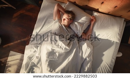 Top View Home: Handsome Young Man Sleeps in His Bed, Sun Shines on Him, He Opens Eyes and Greets New Sunny Day at Home. Joyful Waking Up of a Guy who is Ready for Productive Day. Top Down Above Shot Royalty-Free Stock Photo #2229882503