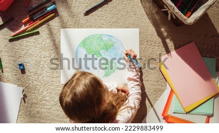 Top View: Little Girl Drawing Our Beautiful Planet Earth. Very Talented Child Having Fun at Home on the Floor, Imagining Our Home Planet as a Happy Place with Clean, Sustainable Living. Cozy Sunny Day