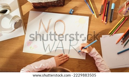 Top View: Little Girl Drawing NO WAR! in Protest against Evil, Greedy People who Bring Only Poverty, Violence and Destruction to Our Beautiful Planet. Young Sad Child Trying to Bring Peace By Her Own