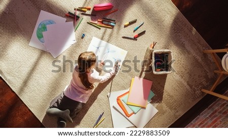 Top View Home: Little Girl Drawing Beautiful Wind Power Turbines Looking Like Flowers. On Sunny Day Smart Child Imagining Planet as a Happy Place with Clean, Sustainable Green Energy for All. Royalty-Free Stock Photo #2229883509