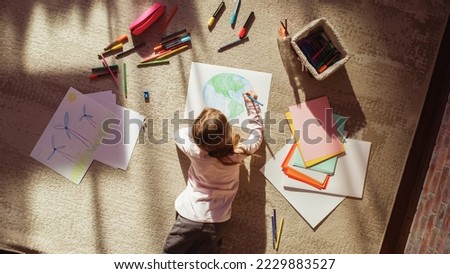Top View: Little Girl Drawing Our Beautiful Planet Earth. Very Talented Child Having Fun at Home, Imagining Our Home Planet as a Happy Place with Clean, Sustainable Living. Cozy Sunny Day.