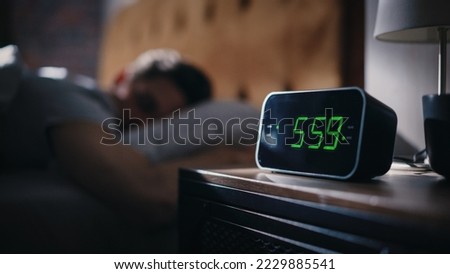 Handsome Man Wakes Up and Turns off Alarm Clock. Proceeds to Have a Productive Day of Work. Stylish Apartment. Focus on the Clock Showing Five Hours and Fifty Nine Minutes in the Morning Royalty-Free Stock Photo #2229885541