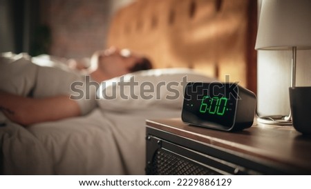 Man Wakes Up and Turns off Alarm Clock. Early Rising Productive Man Ready Start a Day full of New Business Projects, Adventures. Focus on Clock Showing Six O'Clock. Sun is Shining. bedroom Apartment Royalty-Free Stock Photo #2229886129