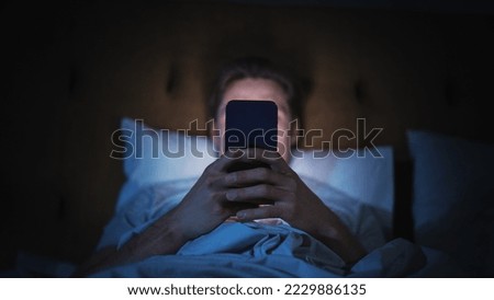 Anonymous Man Uses Smartphone in Bed at Home at Night. Handsome Guy Browsing Social Media, Reading News, Doing Online Shopping Late at Night. Focus on Hand Holding Mobile Phone Covering Face Royalty-Free Stock Photo #2229886135