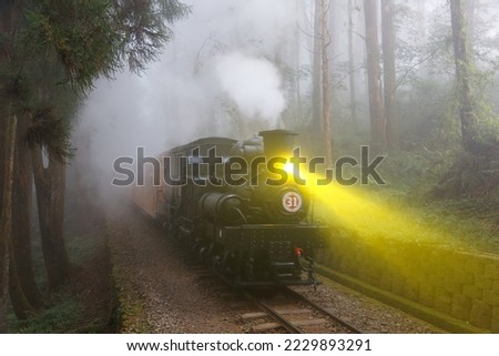 A tourist train, hauled by an antique steam locomotive, traveling thru a forest in the heavy fog, with the track lighted up by the lamp, in Alishan Mountain Resort and Nature Reserve, Chiayi, Taiwan Royalty-Free Stock Photo #2229893291