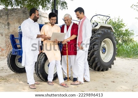 Young man guiding farmer about modern farming techniques using laptop on agriculture field.