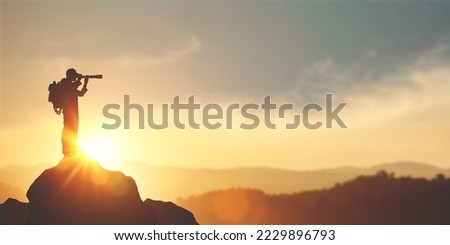 vision for success ideas. businessman's perspective for future planning. Silhouette of man holding binoculars on mountain peak against bright sunlight sky background. Royalty-Free Stock Photo #2229896793