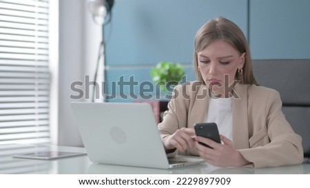 Businesswoman using Smartphone while using Laptop in Office