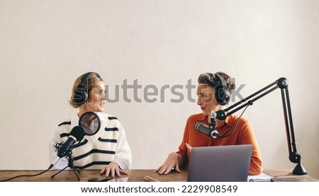 Two female podcasters having a conversation while co-hosting an a show in a home studio. Two women recording an audio broadcast for their social media channel.
