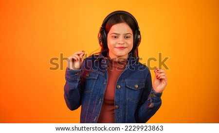 Young woman listening music with wireless headphones on her head, happy teenage girl dancing and enjoying music isolated over colour background