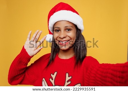 Close up merry little kid teen girl 13-14 years old wear red xmas sweater Santa hat posing do selfie shot pov mobile cell phone isolated on plain yellow background. Happy New Year 2023 holiday concept