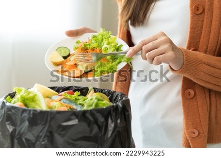 Compost from leftover food, asian young housekeeper woman hand holding cutting board use fork scraping waste, rotten vegetable throwing away into garbage, trash or bin. Environmentally responsible. Royalty-Free Stock Photo #2229943225