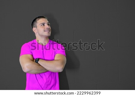 Nice picture with young caucasian male athlete crossing his arms smiling and looking to the side. Confident and positive success concept. Goal achievement. Blank wall, copy space.