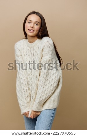 a modest woman is standing full-face on a light background in a white sweater with her hands down holding the sweater with them