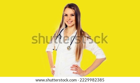 Portrait of friendly smiling young woman doctor with stethoscope on yellow background