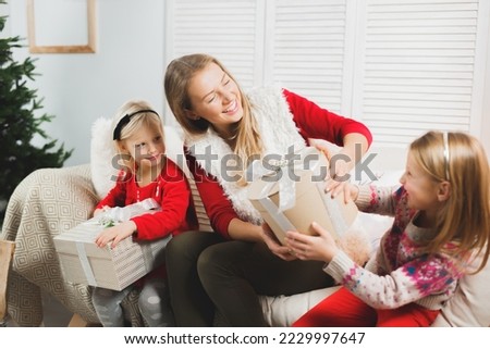 Mother and little kids opening Christmas presents. Living room. Cozy winter evening at home