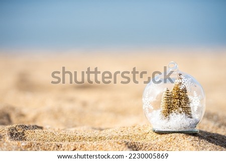 Close up snow globe with golden Christmas tree inside on the beach, blurry background, copy space, soft focus