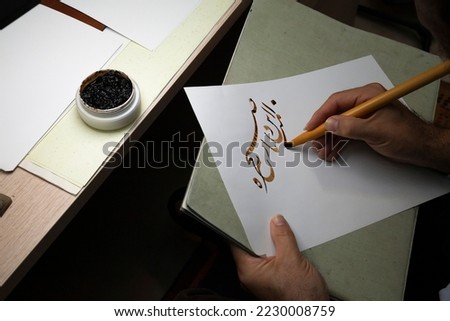 A calligrapher writing with pen and ink. man hands writing arabic calligraphy with ink. Arabic and Persian calligraphy. Written in Farsi, "This dark morning blew again, from where?" Royalty-Free Stock Photo #2230008759