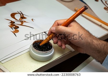 A calligrapher writing with pen and ink. man hands writing arabic calligraphy with ink. Arabic and Persian calligraphy. Writing Nastaliq calligraphy. "Allah God" is written in Arabic in the background