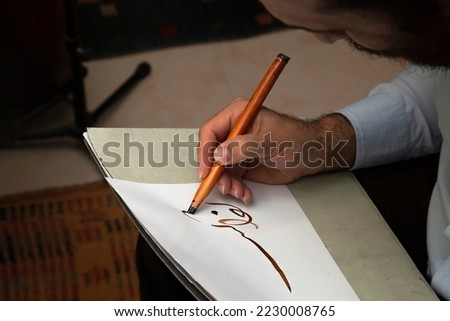 A calligrapher writing with pen and ink. man hands writing arabic calligraphy with ink. Arabic and Persian calligraphy. Writing Nastaliq calligraphy. Abstract and unclear writing. Royalty-Free Stock Photo #2230008765