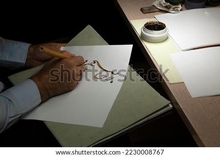 A calligrapher writing with pen and ink. man hands writing arabic calligraphy with ink. Arabic and Persian calligraphy. Written in Farsi, "This dark morning blew again, from where?" Royalty-Free Stock Photo #2230008767
