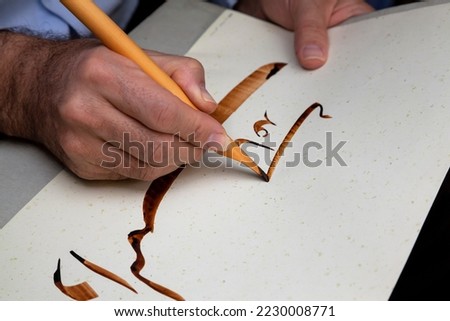 A calligrapher writing with pen and ink. man hands writing arabic calligraphy with ink. Arabic and Persian calligraphy. Writing Nastaliq calligraphy. "Help me" written in Arabic