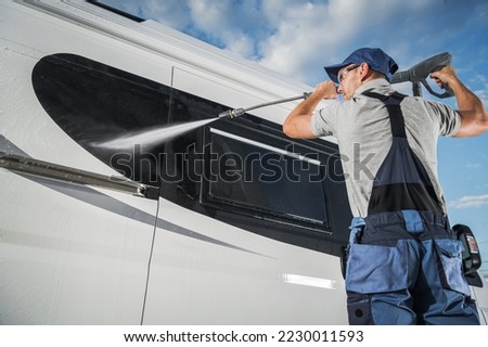 Professional Caucasian Car Detailing Services Worker Cleaning the Exterior of White Recreational Vehicle Using Pressure Washer Machine. Royalty-Free Stock Photo #2230011593