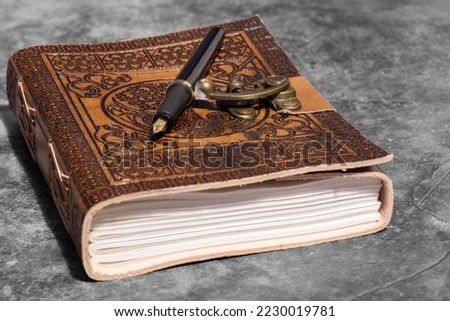 Leather journal, embossed with Celtic tree of life design, with recycled paper and fountain pen. On a dark stone background