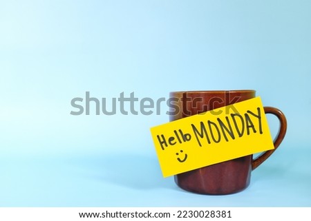 Welcome, hello and happy Monday concept. Selective focus of coffee cup with bright yellow paper note and written message isolated in blue background.