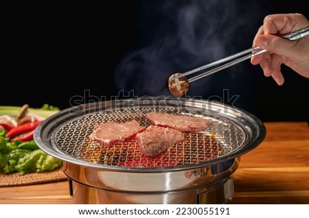 Hand using chopsticks to pick up Mashroom on hot charcoal Asian BBQ food style, Grilled Beef Sirloin meat on the charcoal stove,Korean BBQ style. Royalty-Free Stock Photo #2230055191