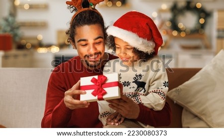 Happy African american curly boy with father opening christmas present, excited  kid  son with loving dad on couch. New Years traditions for families 