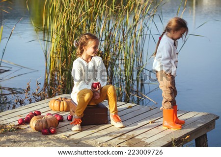 Two cheerful little girls playing on the lake in warm autumn day / Fall lifestyle portrait of children having fun on wooden berth over the river landscape