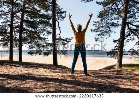 Woman standing in sandy Võsu beach, Estonia. Arms raised, outstreched hands. Positive energy, silhouette, trees. Royalty-Free Stock Photo #2230117635