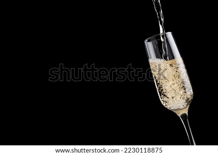 Rich golden flow of fizz champagne pour to wine glass on black background, closeup, detail, copy space. Festive luxury background with holiday drink for restaurant advertisement, card, flyer, design.
