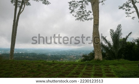 the view of the cloudy sky, trees, mountains and houses photographed from the top of the hill