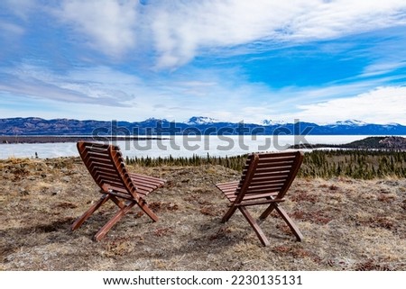 Two chairs vista point overlooking still ice-covered frozen Lake Laberge spring taiga boreal forest landscape of Yukon Territory, YT, Canada Royalty-Free Stock Photo #2230135131