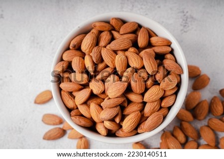 Almonds in white porcelain bowl on white table. Almond concept with copyspace.

