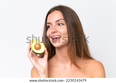 Young caucasian woman isolated on white background holding an avocado while smiling. Close up portrait