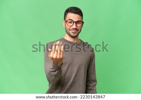 Young handsome caucasian man over isolated background inviting to come with hand. Happy that you came