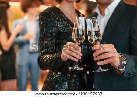 Close up view of champagne glasses. Group of people in beautiful elegant clothes are celebrating New Year indoors together. Royalty-Free Stock Photo #2230157937