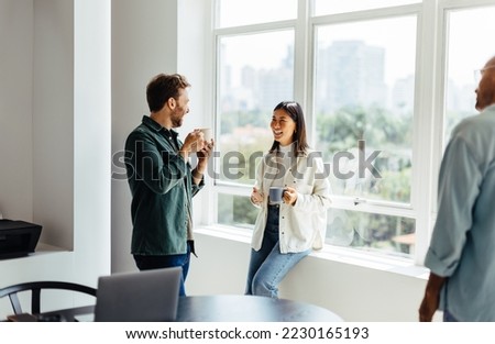Happy business people chatting with each other during a coffee break in an office. Young business people working together in a casual office. Royalty-Free Stock Photo #2230165193