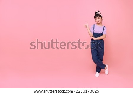 happy Asian girl kid pointing finger to blank space beside isolated on pink background.