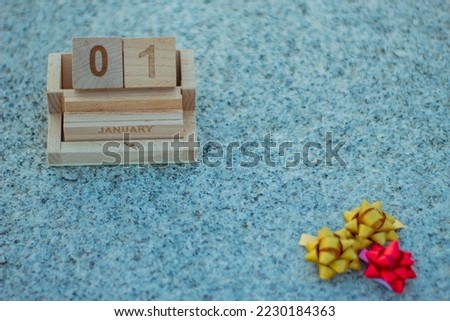 Wooden calendar with the date of the first of January, the New Year's Day with some gift bows with the colors of Christmas.