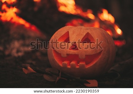 Scary Jack O Lantern halloween pumpkins in darkness on ground among dry leaves at street. Hallows eve decoration funny glow pumpkin with candles on dark background in open air near house