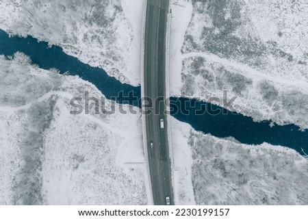 Aerial top view of snow winter road with cars over blue river Royalty-Free Stock Photo #2230199157